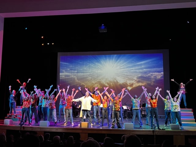 Joseph and the Amazing Technicolor Dreamcoat actors on stage with arms in the air